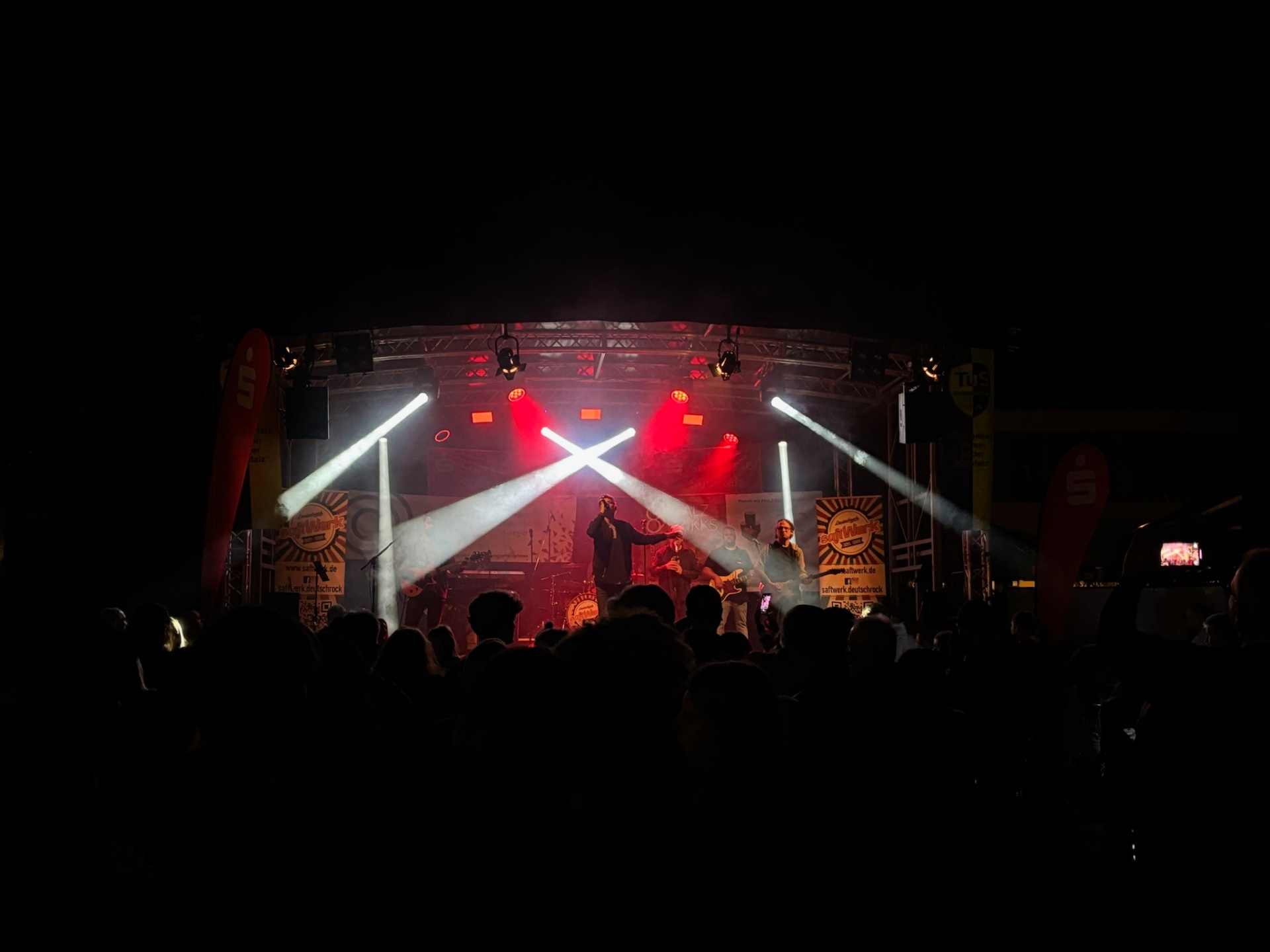 Live-Band auf beleuchteter Bühne mit weißen Lichtstrahlen und Publikum